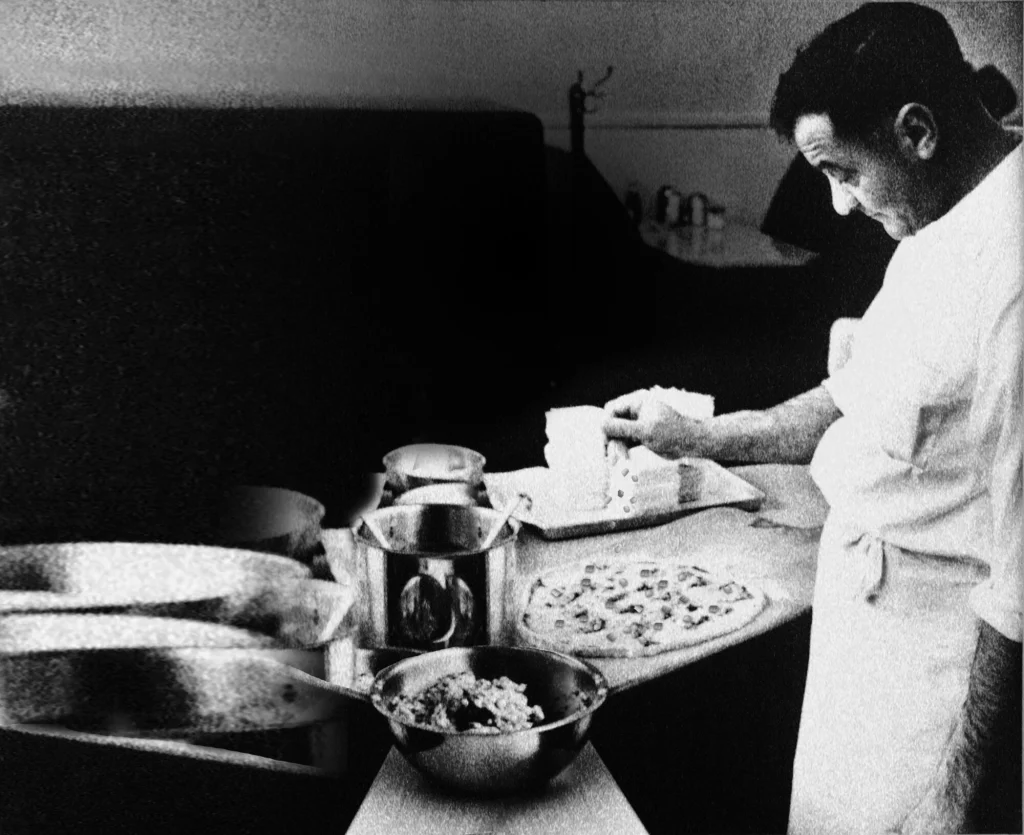 Grandpa Sam Perrella sprinkling toppings onto a freshly made pizza